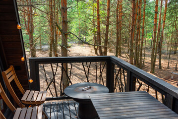 Outdoor deck setup with two wooden chairs and a round table, surrounded by a natural forest area....