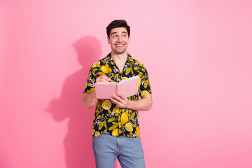 Cheerful young man in tropical print shirt holding a pink notebook against a vibrant pink...