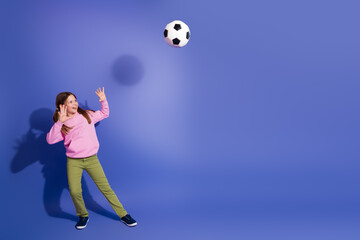 Smiling young girl wearing casual clothes playing with a soccer ball on a vivid colorful blue...