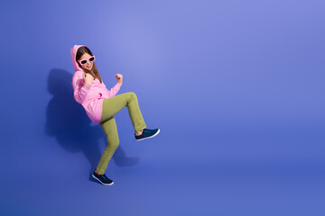 Cheerful young girl in vibrant outfit posing playfully against purple background showcasing fun lifestyle expression