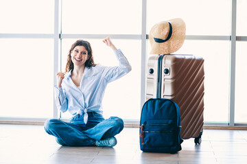 Young woman traveler sitting on floor with luggage at airport terminal, expressing excitement for a...