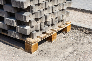 Concrete bricks stacked on a wooden pallet at a construction site during daytime near a gravel area