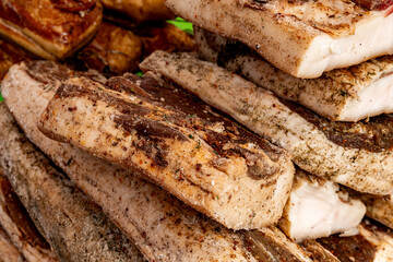 Freshly prepared slabs of seasoned pork belly stacked high in a bustling market in mid-afternoon,...