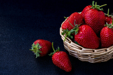 Fresh strawberries in a wicker basket placed on a dark surface showcasing vibrant red fruit with green leaves