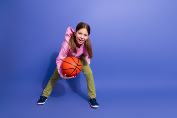 Adorable young girl smiling while holding a basketball, dressed in colorful casual wear, isolated...