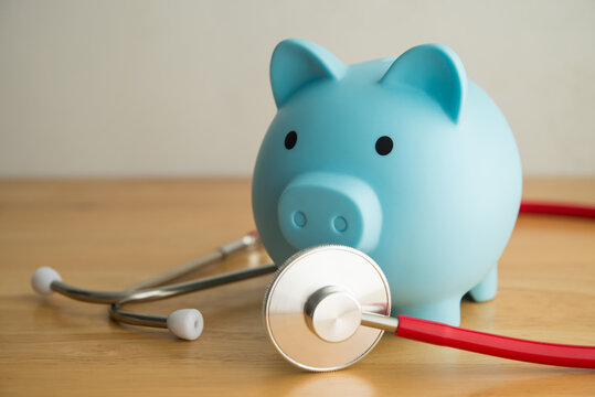 Blue piggy bank and red stethoscope on wooden table with white wall background copy space. Health savings account (HSA), healthcare, life insurance or personal financial checkup and so on concept.