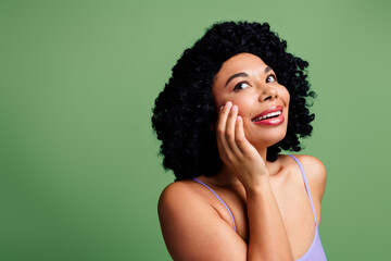 Charming woman posing with natural curly hair in front of a green background embracing self-care...