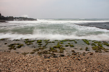 Misty seascape with blurred waves and a mossy, rocky shore at low tide.
