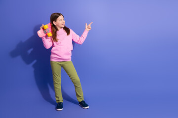 Adorable schoolgirl holding a pink skateboard on a vibrant purple background, expressing fun and enthusiasm