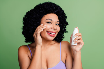 Smiling woman with curly hair applying skincare lotion while promoting self-care and wellness on a...