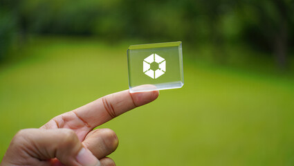 A Hand Holding a Transparent Cube with a White Hexagon Design Against a Green Background, Illustrating Innovation, Technology, and the Interconnectedness of Ideas