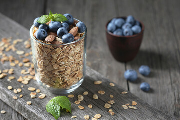 Granola and fresh blueberries in glass bowl over old wood background.