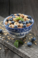Granola with nuts and fresh blueberries in glass bowl over old wood background.