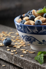 Granola with nuts and fresh blueberries in glass bowl over old wood background.