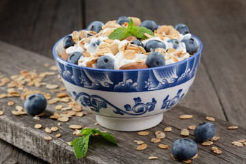 Granola with yogurt and fresh blueberries in glass bowl over old wood background.