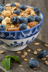 Granola with nuts and fresh blueberries in glass bowl over old wood background.