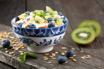 Granola with kiwi fruit, yogurt and fresh blueberries in glass bowl over old wood background