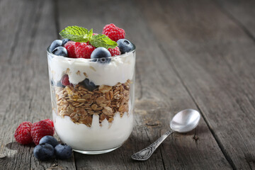 Granola with yogurt, fresh blueberries and raspberries in glass over old wood background.
