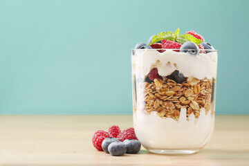 Granola with yogurt, fresh blueberries and raspberries in glass on wood background