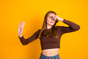 Young woman pinching her nose while expressing discomfort against a vibrant yellow background