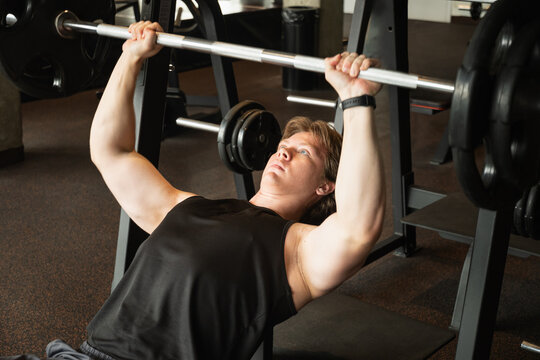 Sporty caucasian man or bodybuilder exercising bench press at fitness center. Male athlete lifting weights.