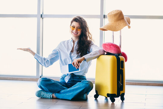 Young woman sitting in an airport with a suitcase and passport ready for travel and vacation adventure