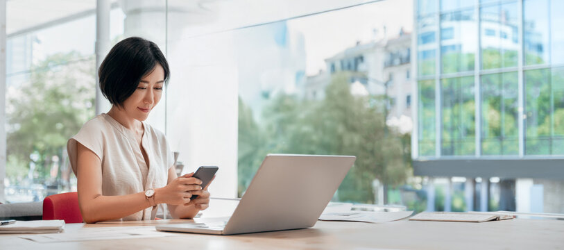 Young eastern successful business woman manager ceo using cell phone mobile. Smiling asian mature female businesswoman holding smartphone in office for trading working call online. Banner, copy space