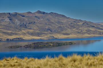 Fototapeta premium Deep blue waters embrace golden highland hills at Lagunillas Lake near Puno — a serene Andean sanctuary of beauty and calm