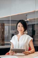 Vertical portrait at camera Asian mature woman ceo manager using tablet for business work,...