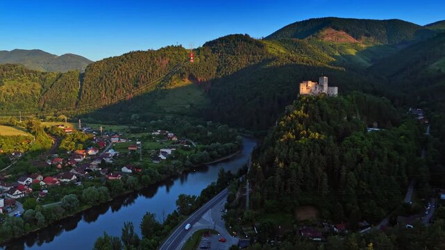 Countryside in the mountainous area of Slovakia. Aerial view on the village situated on the bank of the river. Old castle on top of the green rock.
