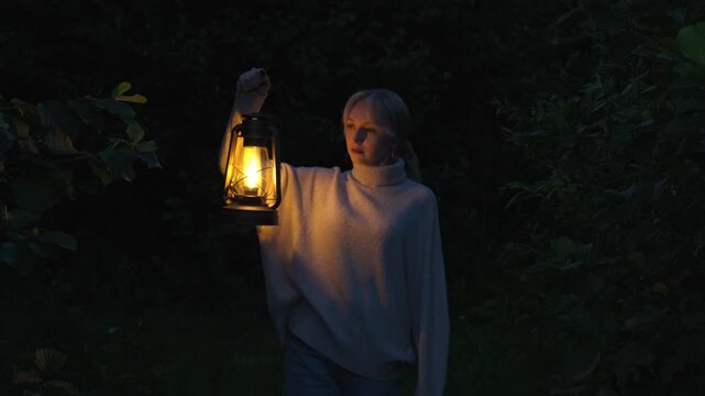 A lonely, anxious woman walks through the forest at night with a burning kerosene lamp in her hand. The concept of anxiety, arousal and fear.