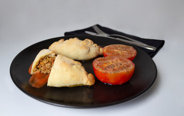 Argentinian tuna empanadas with tomato sauce and 2 seasoned tomato halves.