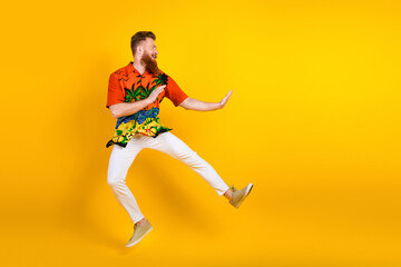 Young man in tropical shirt joyfully jumping against vibrant yellow background, exuding energy and summer vibes