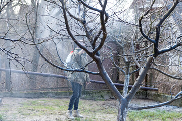 A woman works in the spring garden and spray with a rechargeable sprayer chemicals against pests