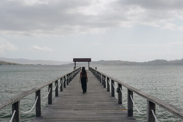 Obraz premium Elegant young Asian woman enjoying holiday while striking a pose on a bridge in Golo Mori harbor.