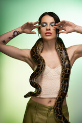 Young woman captivates with beauty and poise while posing with a snake in an artistic setting