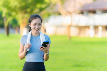 Happy fitness girl in headphones looking at smartphone while standing outdoors before exercising,...