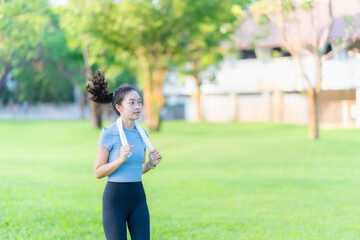 Asian woman stretches her body and neck after jogging at a city park, enjoying outdoor sports...