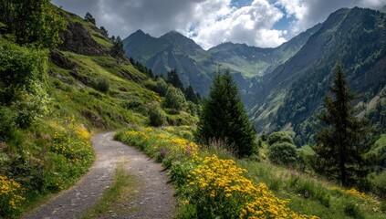 Obraz premium Winding mountain path through wildflowers. A gravel path winds through a valley of wildflowers, framed by lush green hills and towering mountains. Clouds gather in the sky