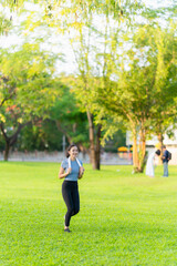 Asian woman stretches her body and neck after jogging at a city park, enjoying outdoor sports practice.
