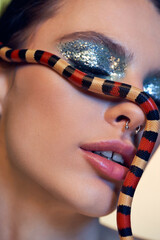 Young beautiful woman elegantly poses with a colorful snake across her face in a whimsical setting