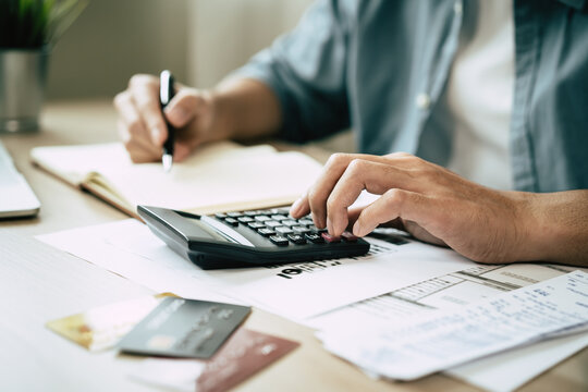 Deduction planning, debt asian accountant hand using calculator to calculating money balance from bill and income, cost budget expenses for pay money form personal individual on table at home.