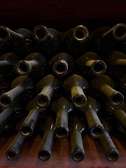 Wine cellar bottles: A tightly packed stack of empty, dark wine bottles is shown in a cellar,...