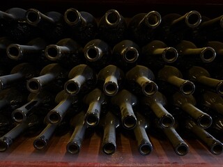 Wine cellar bottles: A tightly packed stack of empty, dark wine bottles is shown in a cellar,...