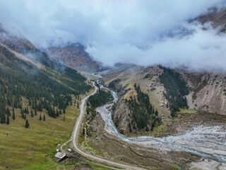 An aerial view of a remote mountain valley enveloped in low clouds, showing a dirt road running...