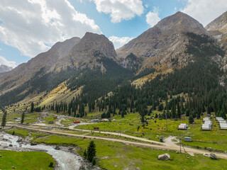 A view of a traditional yurt camp and small buildings nestled in the green Barskoon valley, with a...
