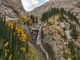 A picturesque scene of a waterfall in a rocky mountain gorge, highlighted by the striking contrast...