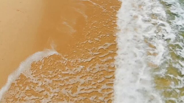 A beach scene with waves washing over the sand creating a textured foamy surface