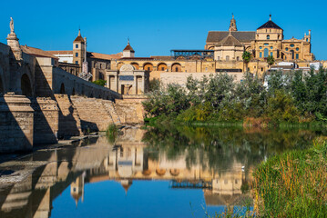 View from the Guadalquivir River of the Roman Bridge and Mosque Cathedral of Córdoba with reflections on the water.