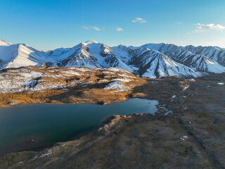 A breathtaking aerial view of an alpine lake in the valley, with the majestic snow-covered Tien...